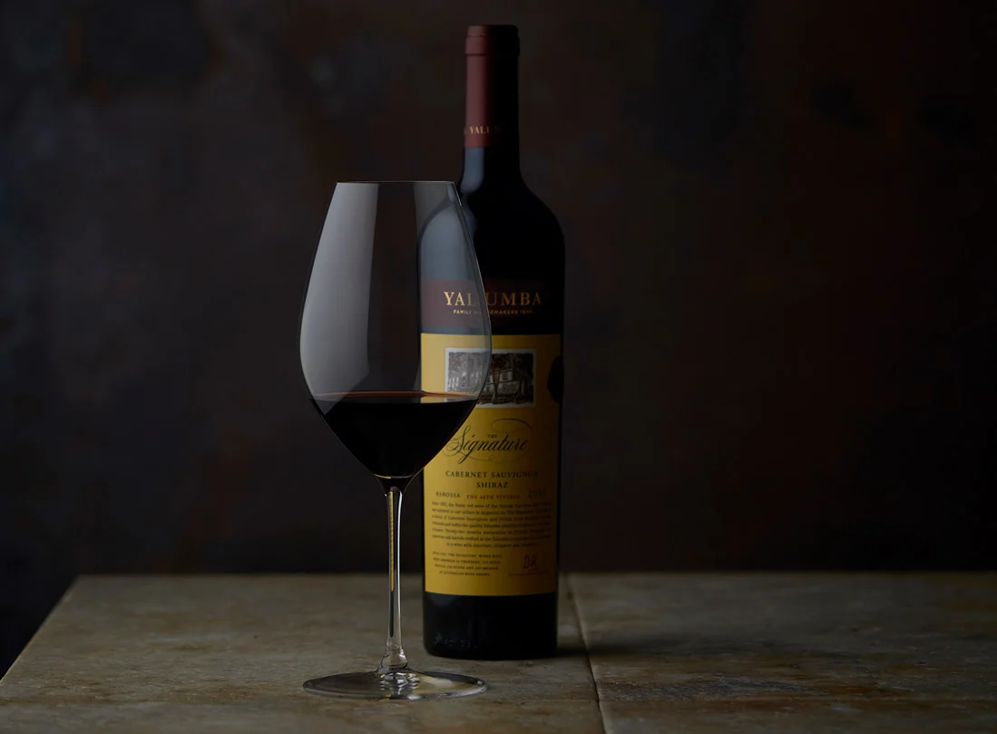 A glass of The Signature sitting in front of it's bottle in a dark room