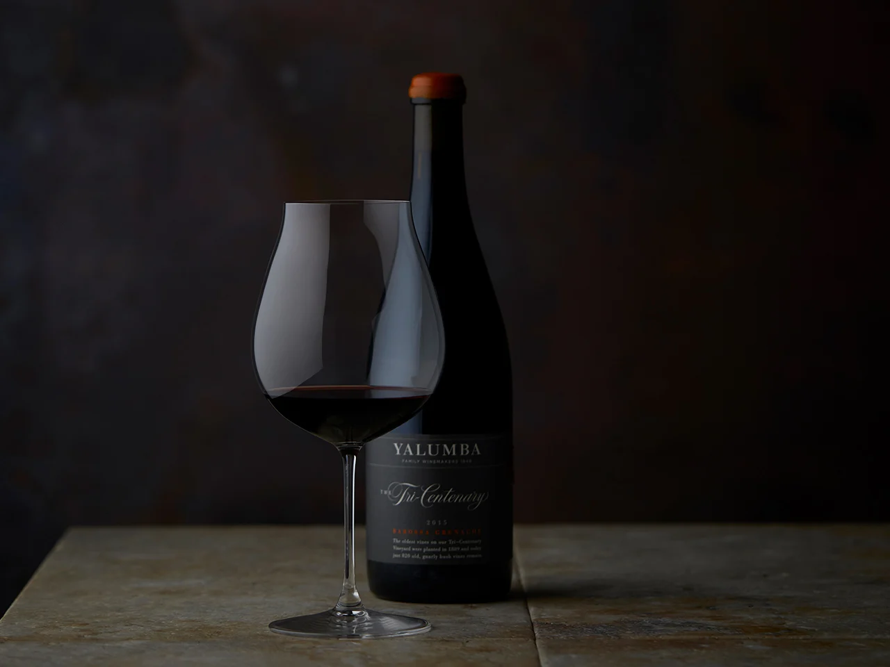 Tri-Centenary wine bottle and filled specialty wine glass on wooden surface