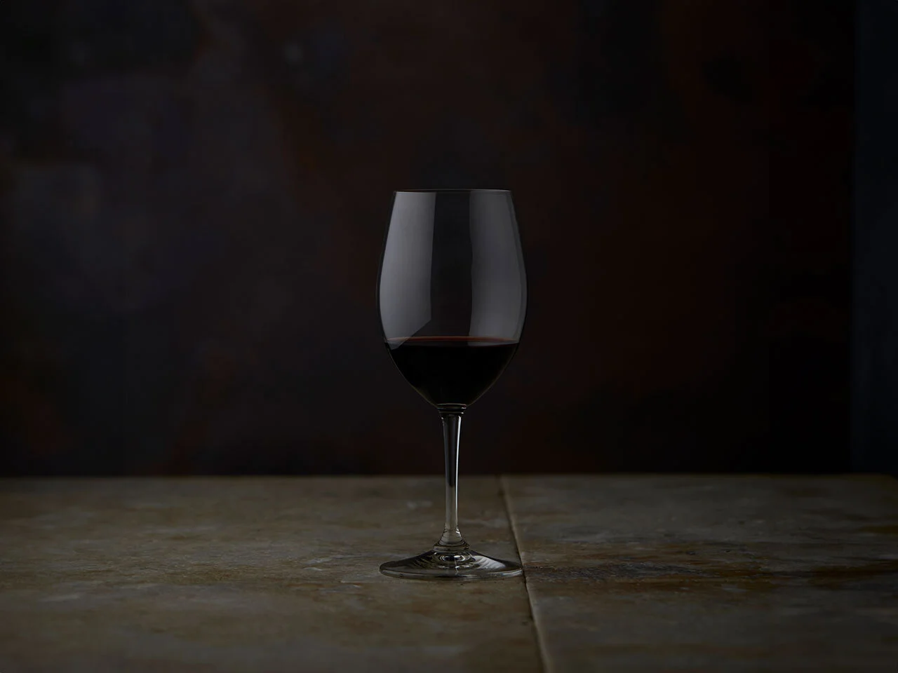 A glass of The Octavius sitting in front of it's bottle in a dark room
