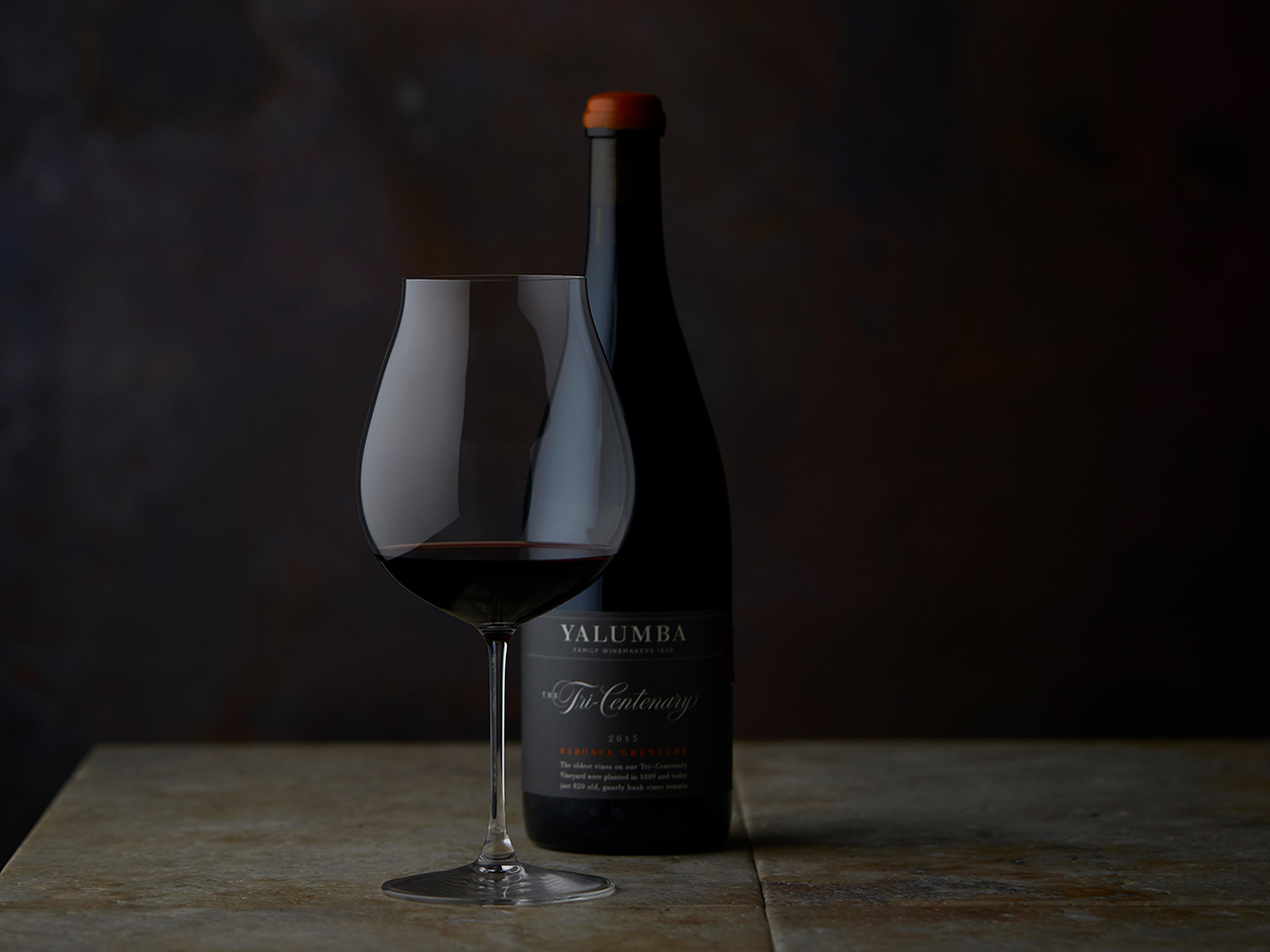 A glass of Yalumbas "Tri Centenary" red wine inside a wine glass, sitting in front of the bottle.
