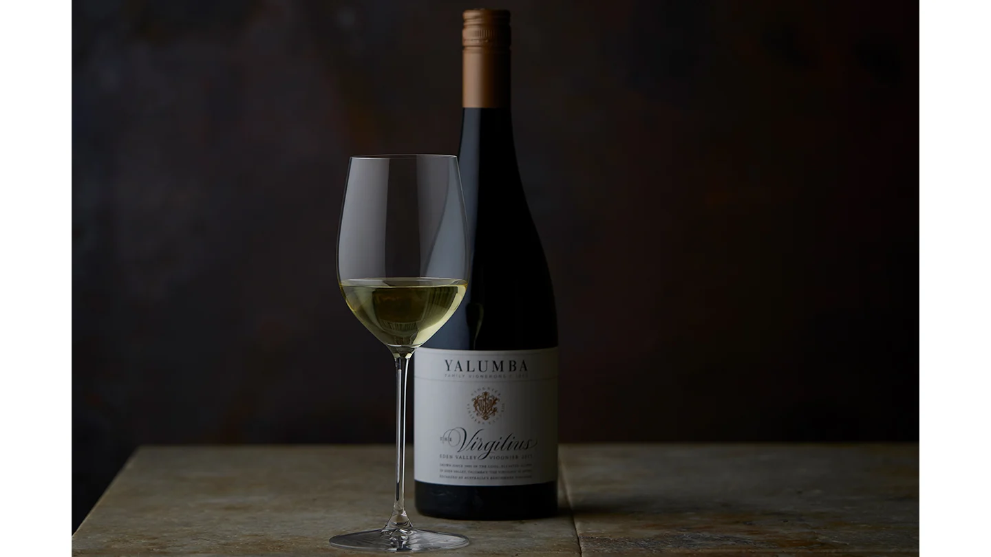 A glass full of The Virgilius with great colouring, sits in front of the bottle in a dim lit room