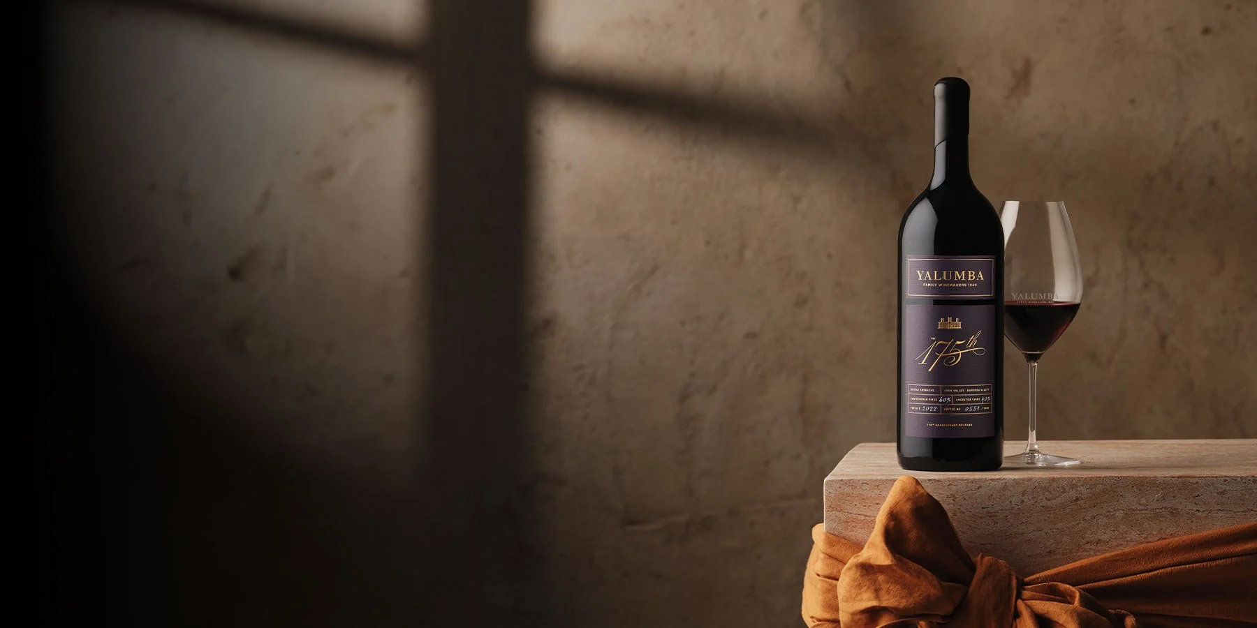 A bottle of 175th Anniversary Wine sits on a block next to a half full wine glass