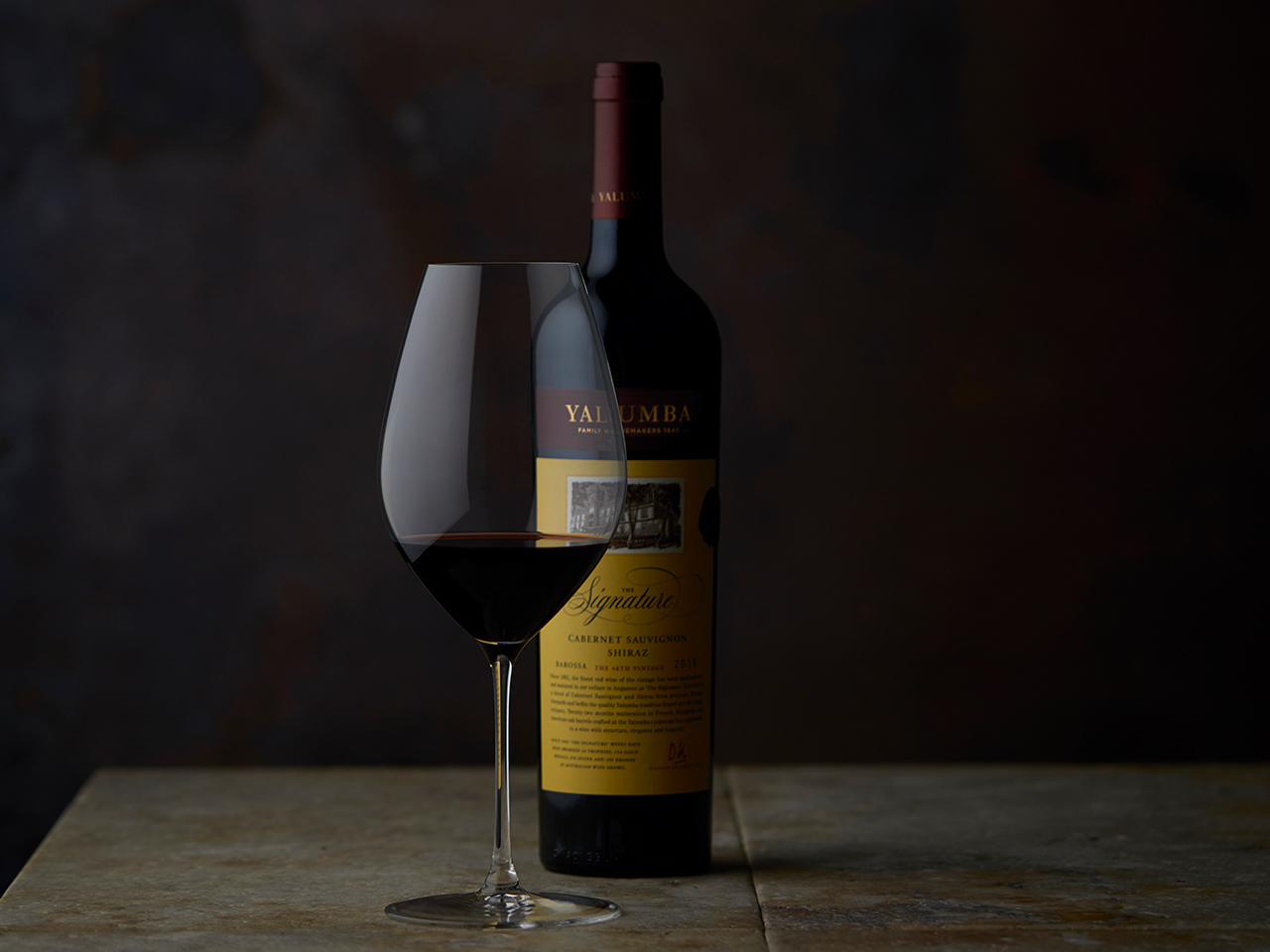 Yalumba Signature wine bottle with filled glass on wooden surface