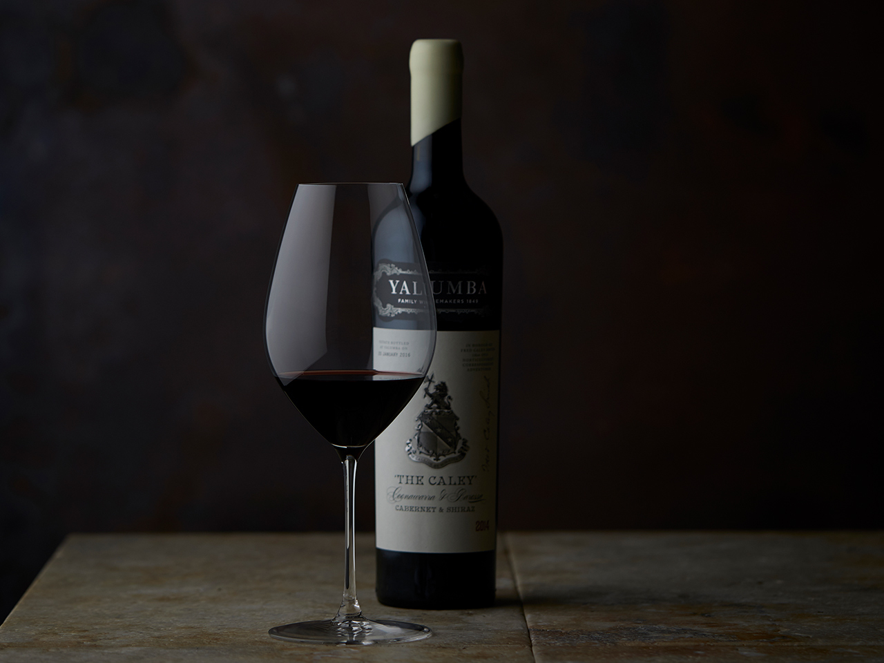 The Caley wine bottle and glass of red wine against dark background