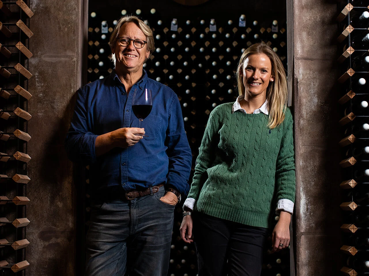 Robert and Jess Hill-Smith enjoying a glass of wine in front of a classy wine rack