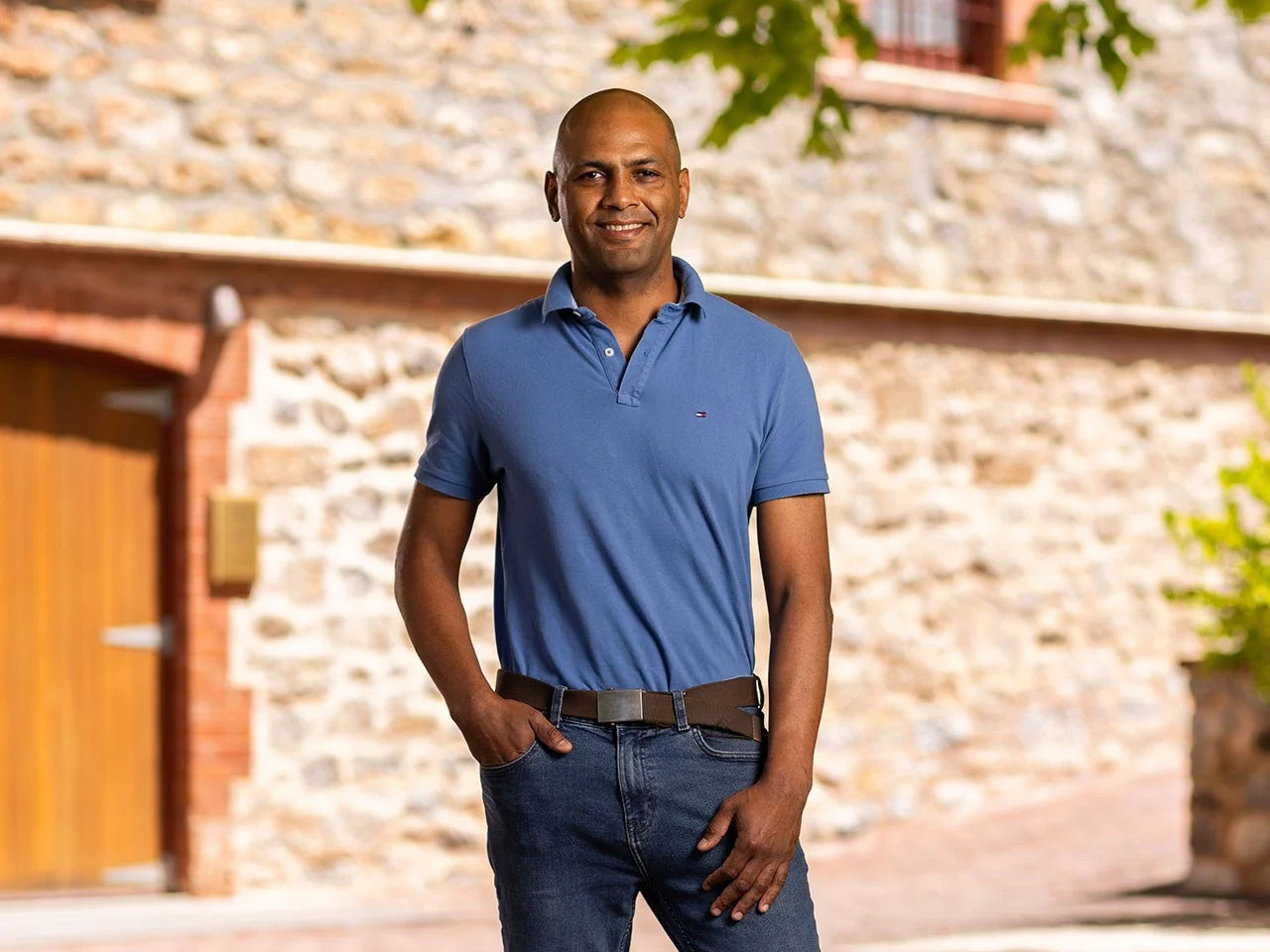 Alexey Doumbouya, Winemaker at Yalumba, standing in blue polo shirt against stone wall at the winery