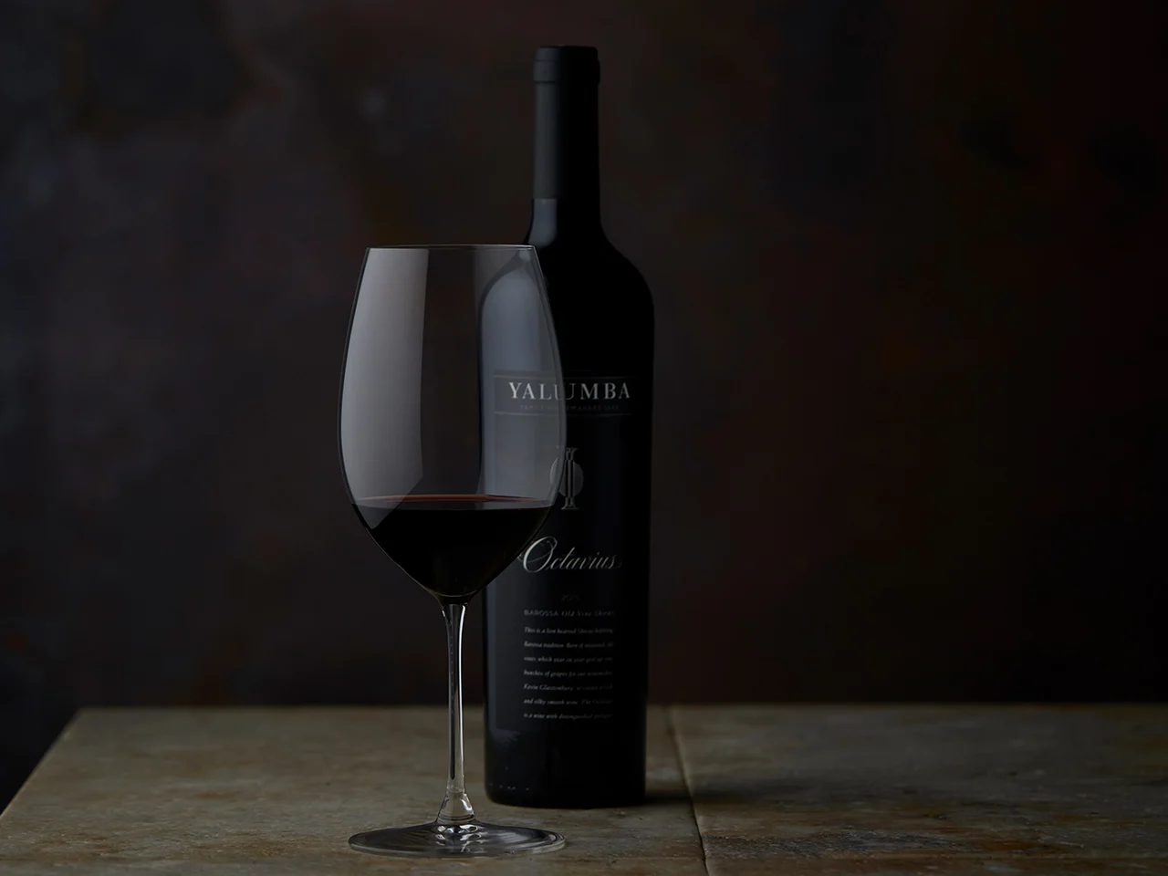 A glass of The Octavius sitting in front of it's bottle in a dark room