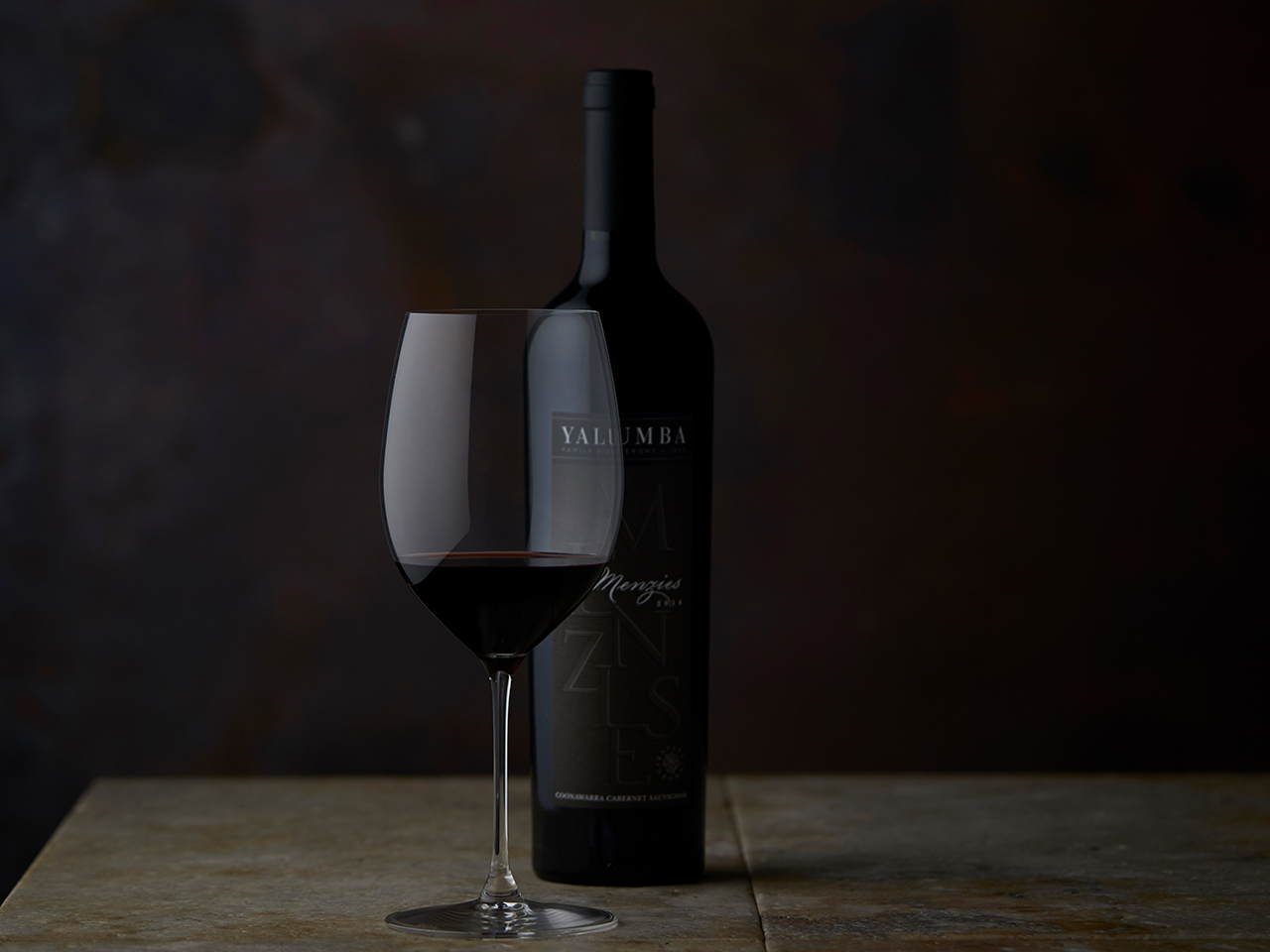 The Menzies wine bottle and filled wine glass on wooden surface