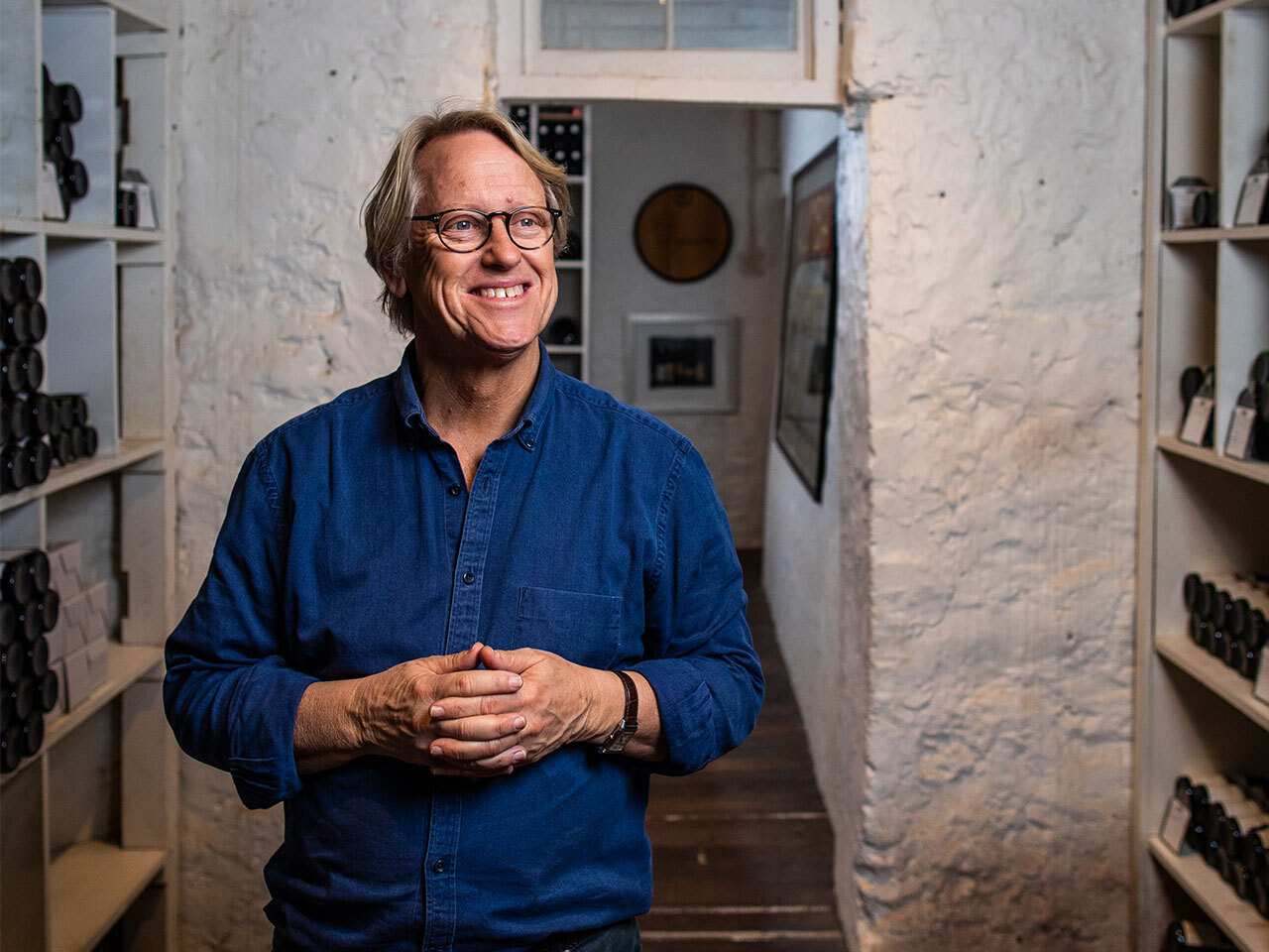 Robert Hill-Smith smiling in blue shirt against stone wall background