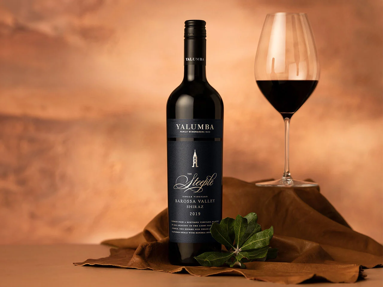 Steeple Vineyard Shiraz bottle with wine glass and autumn leaves against terracotta background