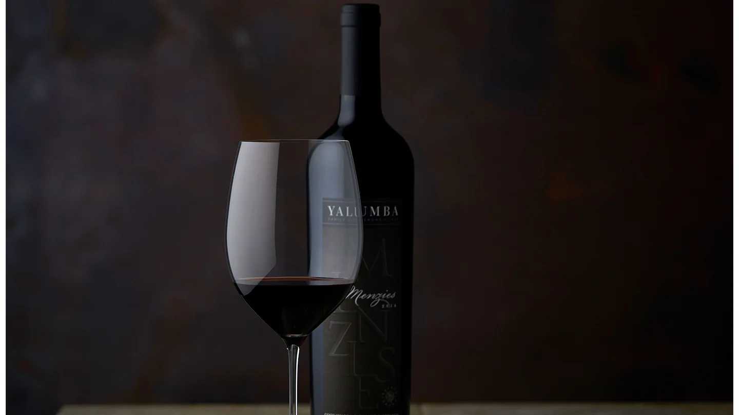 A glass of The Menzies sitting in front of it's bottle in a dark room